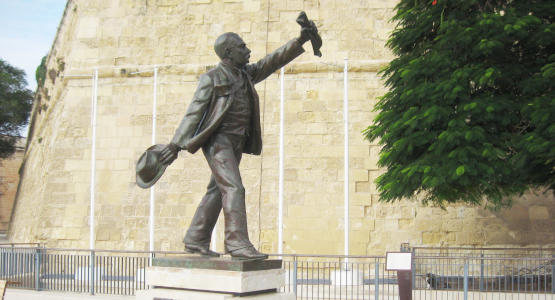 A bonze statue of a running man with a newspaper in his hand in front of a massive stone wall.